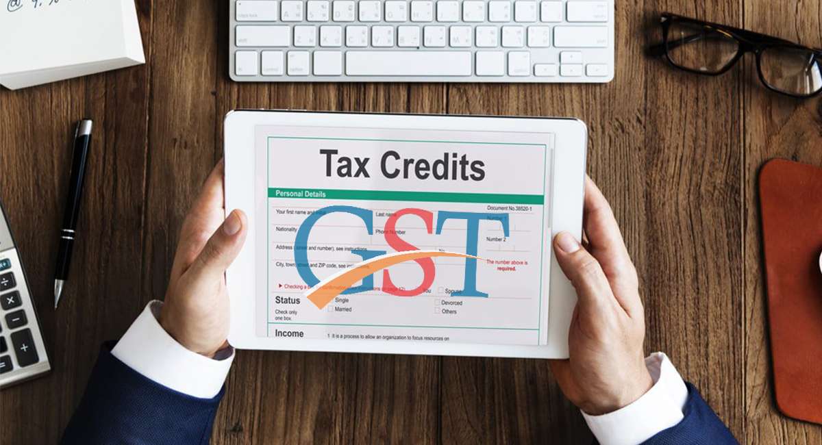 Hand completing GST registration form on computer with organized workspace in background.